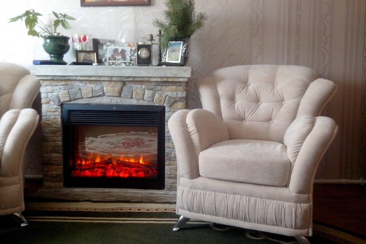 Белое кресло Лера в интерьере гостиной комнаты с камином